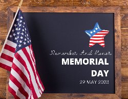 chalkboard on a wooden background with american flag and star and the words, remember and honor Memorial Day 29 May 2023 
